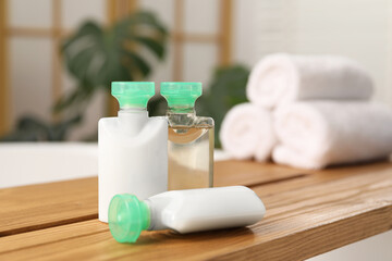 Fototapeta na wymiar Wooden tray with mini bottles of cosmetic products on bath tub in bathroom