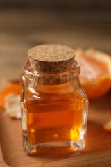 Bottle of tangerine essential oil and peeled fresh fruit on wooden tray, closeup