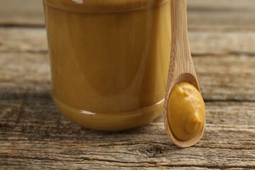 Jar and spoon with tasty mustard sauce on wooden table, closeup