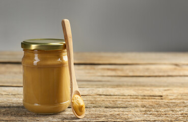 Jar and spoon with tasty mustard sauce on wooden table, space for text