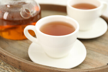 Aromatic tea in cups and teapot on wooden tray, closeup