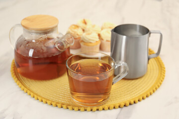Aromatic tea in glass teapot, cup and pitcher on white marble table