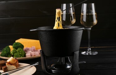 Dipping piece of ham into fondue pot with melted cheese on table