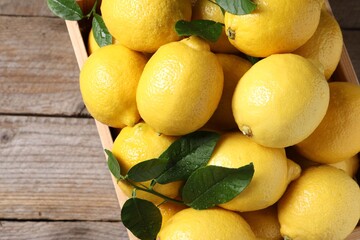 Fresh lemons and green leaves in crate on wooden table, top view