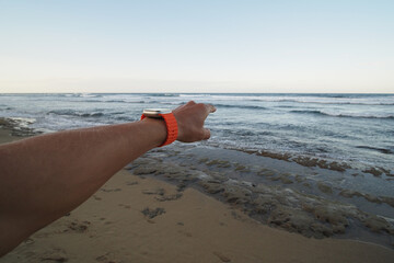 Male hand wearing smartwatch with index finger pointing to something in ocean.