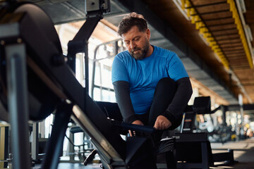 Mature athlete preparing to exercise on rowing machine in gym.