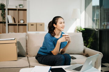 Asian Business woman Talking on the phone and using a laptop with a smile while sitting on sofa