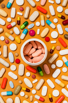  Medicine bottle full with tablet pills on orange background covered in pills