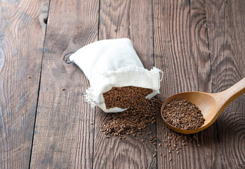 Canvas bag with flax seeds, Wooden spoon with flax seeds on a wooden background.