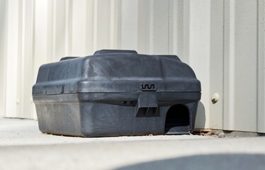 Rat bait station by a wall outdoors, front view at ground level. Common pest control solution for...