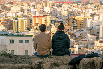 dos chicos jóvenes sentados observando toda la ciudad desde un mirador en la montaña 