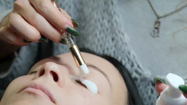 Close-up of washing and degreasing eyelashes before lamination or eyelash extension procedure. Makeup artist and client of a beauty salon.