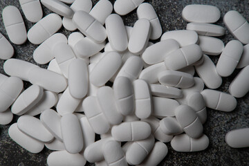 Big pile of white pills on rustic concrete like background.