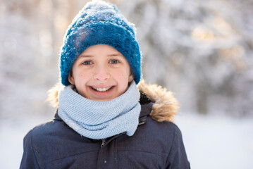 Fototapeta na wymiar portrait of a happy 11 year old European boy with gray eyes, wearing a hat and knitted scarf, snowy winter, outside
