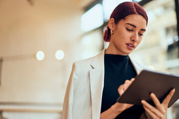 Close-up of a red-haired elegantly dressed woman, using a digital tablet.