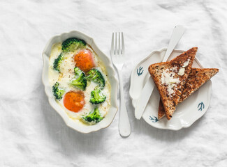 Delicious breakfast, brunch - baked eggs with broccoli and mozzarella and wholegrain toast with butter on a light background, top view