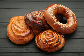 Bakery - various kinds of breadstuff. Bread rolls, bagel, sweet bun on black wooden background. Space for text