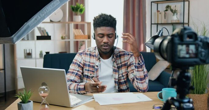 Man Blogger In Headphones Sitting In Front Of Camera In Home Office During Recording New Vlog For His Audience