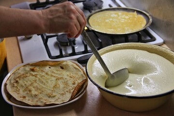 cooking pancakes in a frying pan at home, first person and side view. a frying pan in the hands of a woman and in the other hand a ladle with dough for pancakes