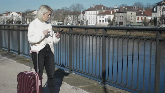 The girl is travelling alone. in a foreign city with a suitcase looking for a hotel on the phone. Lost in the city.