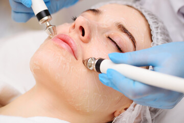 cosmetologist conducts microcurrent facial therapy for a young woman using a device in a beauty...