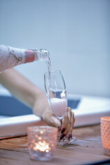 Person pouring wine into a glass on a table with a lit candle in the background, creating a cozy atmosphere.