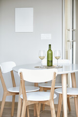 Modern dining room with white table, wooden chairs, wine bottle, and two glasses.