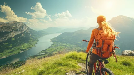 Poster Young athletic woman on top of a mountain with a bicycle and enjoying the view of the stunning valley landscape. © Evgeniia
