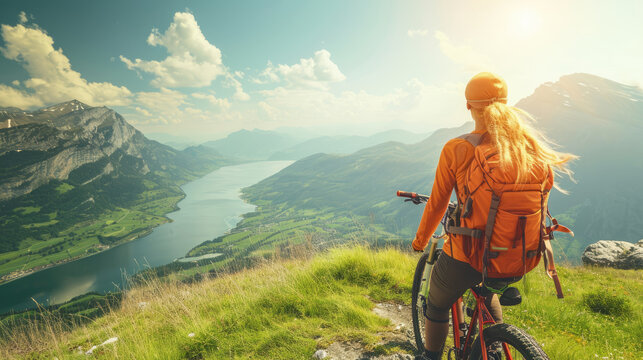 Young athletic woman on top of a mountain with a bicycle and enjoying the view of the stunning valley landscape.