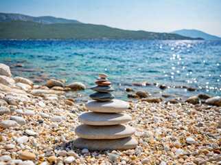 Small cairn from beach rocks, with beautiful landscape of Croatia behind, Croatia coast, sea and rocks in water.