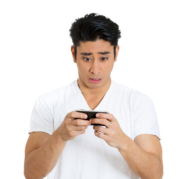 Closeup portrait anxious young man looking at phone seeing bad news or photos with scared emotion on his face isolated on gray wall background. Human emotion, reaction, expression