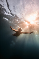 Person swimming underwater with sun rays shining through the surface.