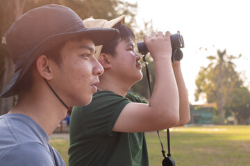 Asian teenboys learning nature by using binoculars to watch birds and insects in public park during...