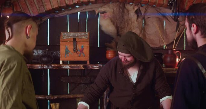 Merchant sells goods to adventurers in tavern. Positive seller with overweight makes trading deal with pilgrim guests in medieval inn. Buy artefacts