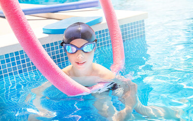 Active child (boy) in cap, sport goggles ready to learns professional swimming with swim noodles...