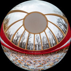 Wide-angle view of the inside of a gazebo with yellow columns and a red bench. Round photo in...
