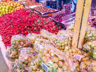 Guavas, strawberries and grapes on shelf in Mexican market, dried fruits and cherries in background, wide variety of fresh seasonal fruits. Retail street sale concept