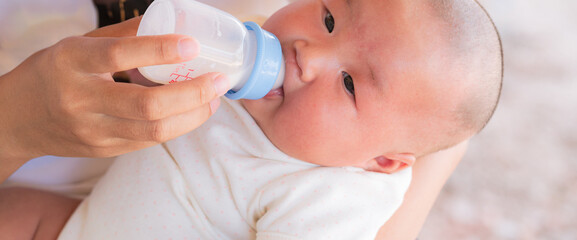 loving mother feeding her little boy child with milk baby bottle at home, portrait infant Baby eating, drinking powdered milk, looking at camera