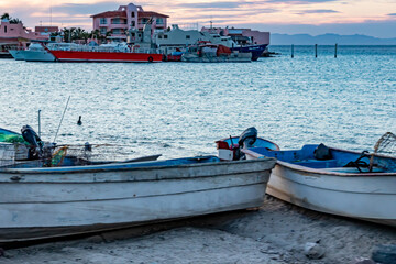 Closeup of two motor boats on beach, blurred in foreground, bay sea, buildings and boats in...