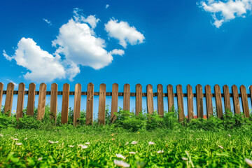 Fototapeta na wymiar Garden fence with green grass and blue sky at summer day, Wooden fence to protect the backyard