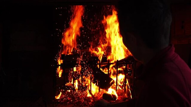 Man put wood into the fire and flames of fireplace. Slow motion video