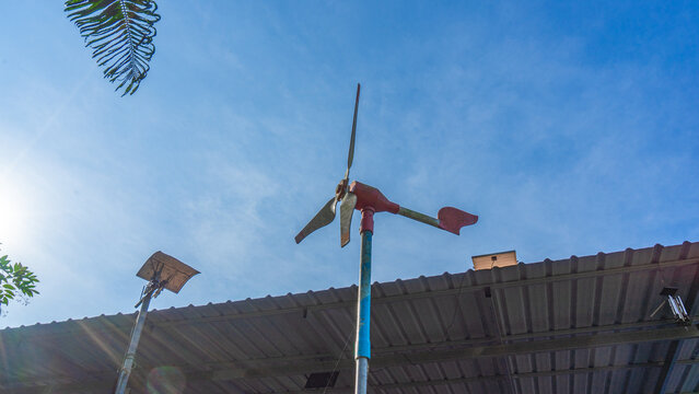 photos of things building A small old windmill pole shaped like a red airplane made of steel. It stands tall above the zinc roof. The background is a bright sky during the day. There are lush green 