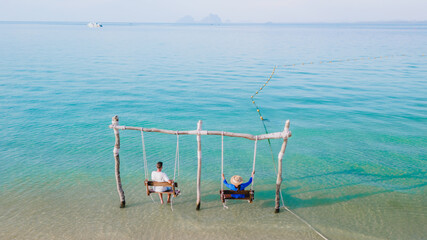 a couple of men and woman on a swing at the beach of Koh Muk Thailand