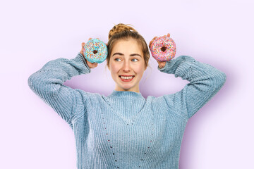 Confused young cheerful woman has sweet tooth laughs, girl holds delicious glazed doughnuts...