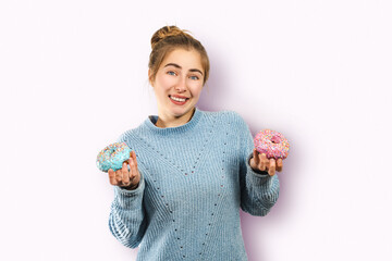 A young funny hungry woman with an embarrassed smile hopelessly chooses donuts instead of a diet isolated over pink background, unhealthy nutrition fast food sweets concept, from Monday go on a diet