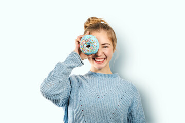 Young positive smiling laughing woman covers one eye with a blue donut, having fun, playing with...