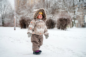 Fototapeta na wymiar Cute child toddler walks in a snowy winter park