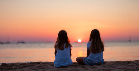 Fototapeta premium girls sitting watching a sunset at the sea