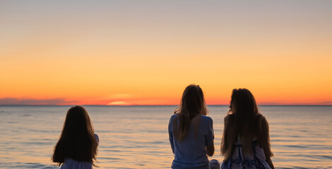 girls sitting watching a sunset at the sea