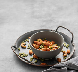 Mix of nuts. Almonds, cashews and pumpkin seeds in a bowl on a gray background with napkin.